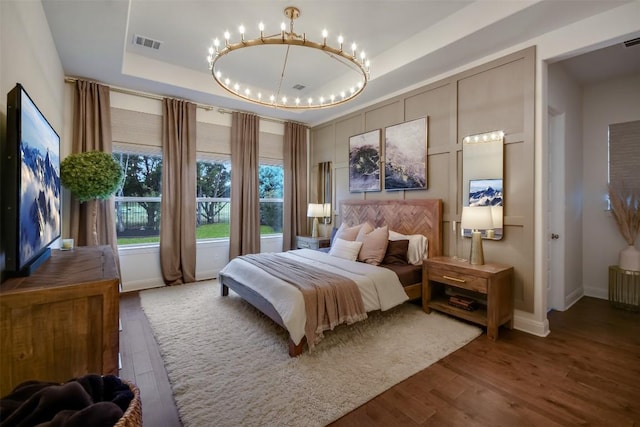 bedroom featuring a chandelier, wood finished floors, visible vents, baseboards, and a raised ceiling