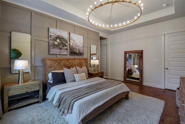 bedroom featuring a raised ceiling, dark wood finished floors, and baseboards