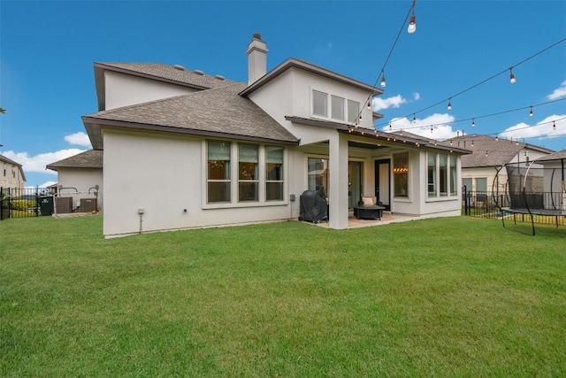 rear view of property featuring a patio area, a trampoline, fence, and a lawn