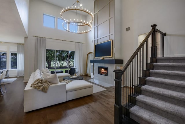 living room with dark wood-style flooring, a fireplace with flush hearth, visible vents, stairway, and an inviting chandelier