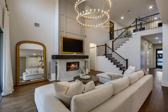 living area with visible vents, a towering ceiling, stairway, wood finished floors, and a fireplace