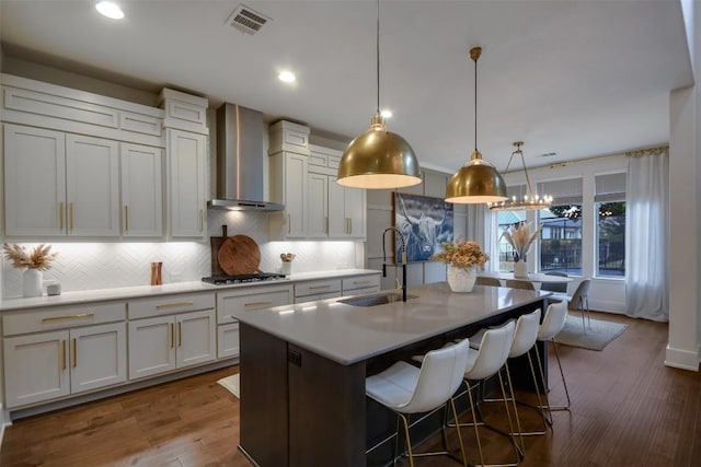 kitchen with light countertops, a center island with sink, a sink, and wall chimney exhaust hood