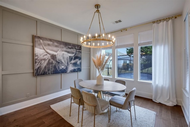 dining room with dark wood-type flooring, visible vents, a decorative wall, and a notable chandelier