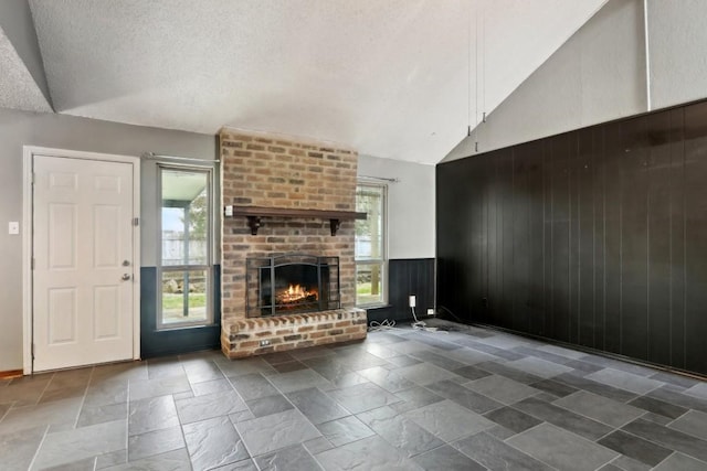 unfurnished living room featuring a fireplace, high vaulted ceiling, a textured ceiling, and wood walls