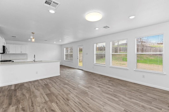 unfurnished living room featuring sink, light hardwood / wood-style floors, and a wealth of natural light