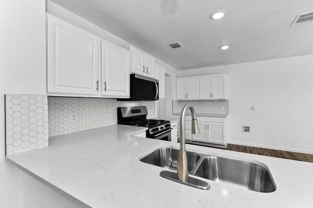 kitchen with appliances with stainless steel finishes, white cabinetry, sink, decorative backsplash, and light stone counters