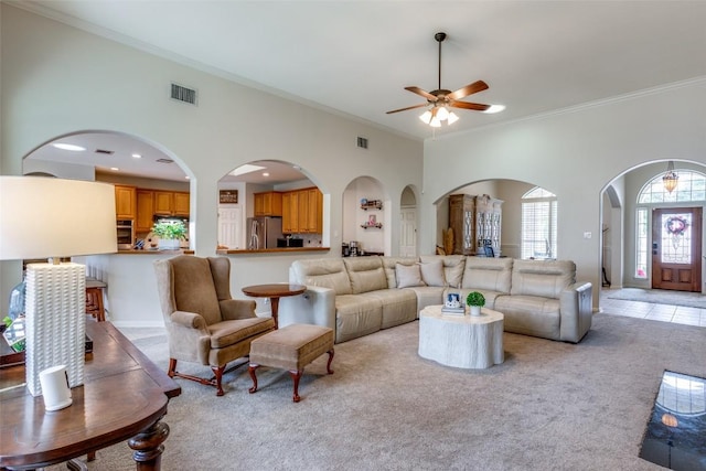 carpeted living room featuring a towering ceiling, ornamental molding, and ceiling fan