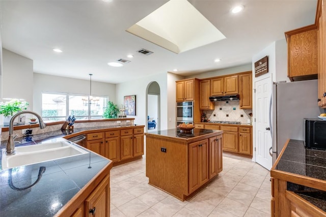 kitchen with a kitchen island, appliances with stainless steel finishes, tasteful backsplash, sink, and hanging light fixtures