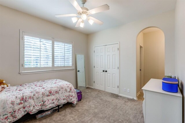 bedroom featuring a ceiling fan, arched walkways, baseboards, a closet, and carpet flooring