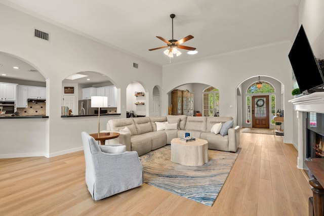 living area with crown molding, a lit fireplace, a ceiling fan, and light wood finished floors