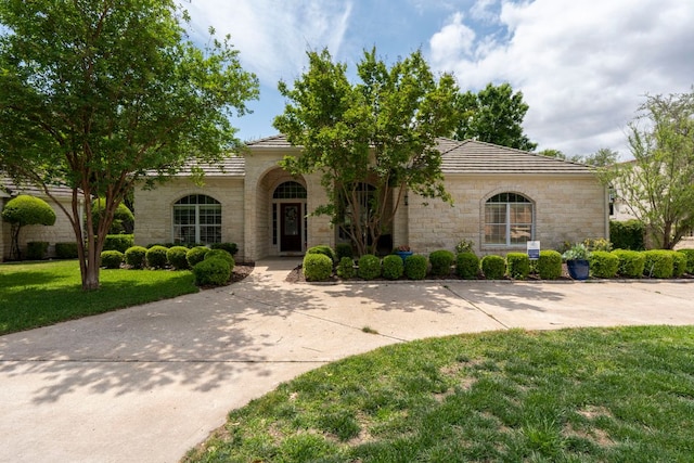 mediterranean / spanish-style home with a tile roof, a front yard, and stone siding