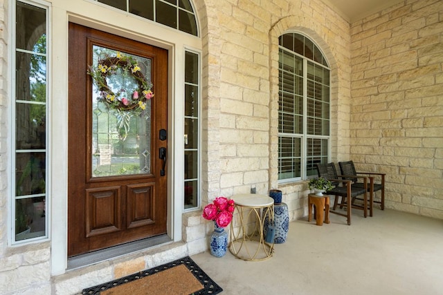 doorway to property with a porch, brick siding, and stone siding