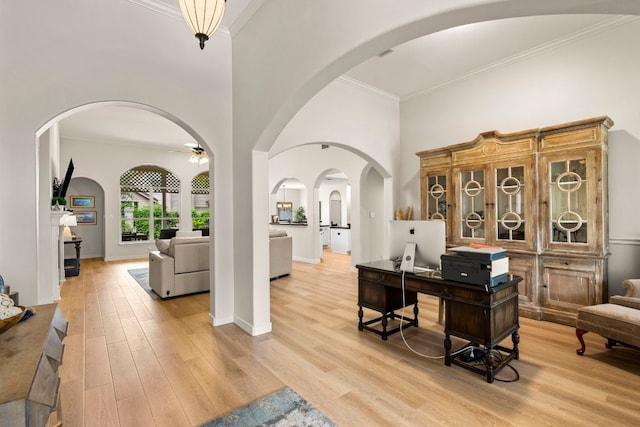 office area featuring a ceiling fan, a towering ceiling, arched walkways, light wood finished floors, and ornamental molding