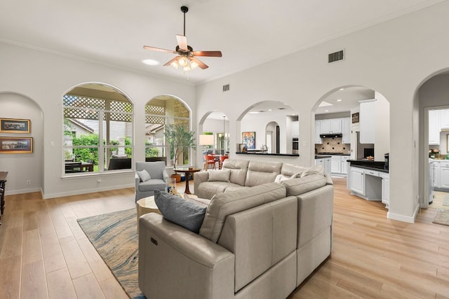 living area featuring a ceiling fan, visible vents, ornamental molding, and light wood-style flooring
