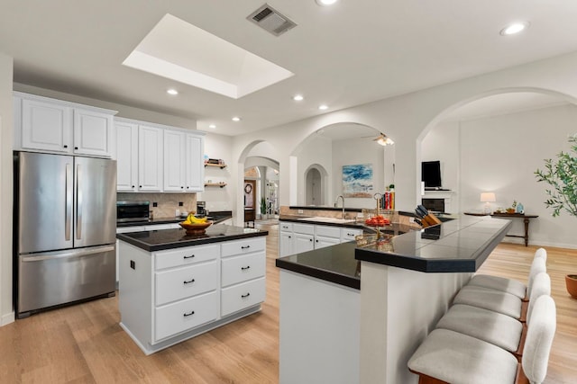 kitchen with freestanding refrigerator, dark countertops, a large island, arched walkways, and light wood finished floors