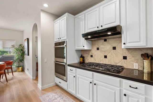 kitchen featuring dark countertops, baseboards, gas cooktop, stainless steel double oven, and under cabinet range hood