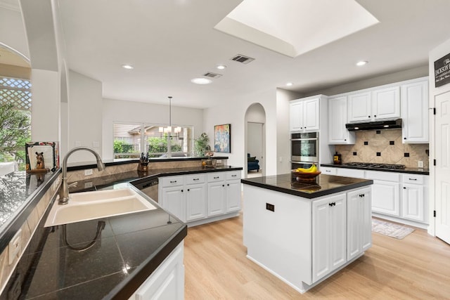 kitchen with appliances with stainless steel finishes, a sink, arched walkways, under cabinet range hood, and visible vents