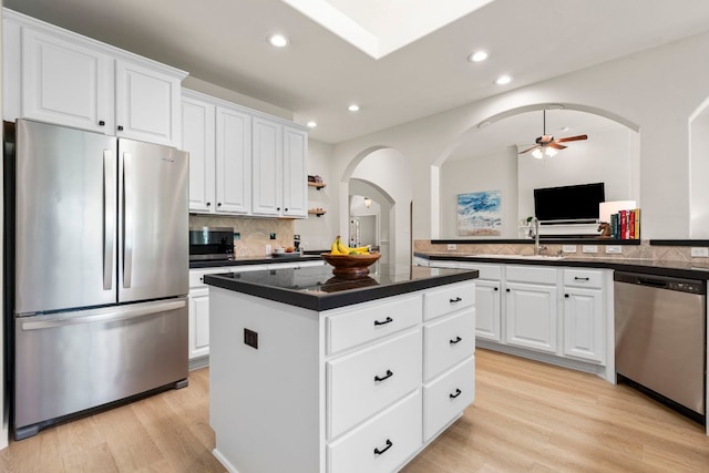 kitchen featuring a ceiling fan, dark countertops, a center island, arched walkways, and stainless steel appliances