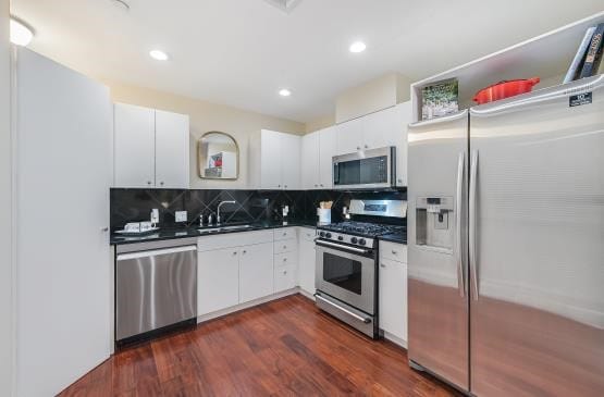 kitchen featuring appliances with stainless steel finishes, dark countertops, a sink, and white cabinetry