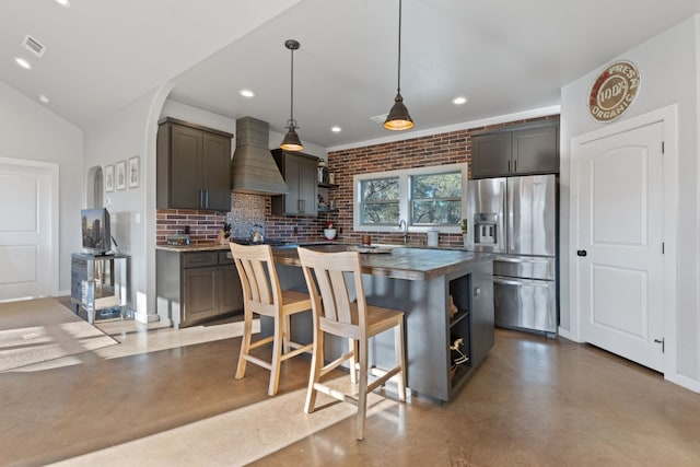 kitchen with a breakfast bar, hanging light fixtures, a center island, custom range hood, and stainless steel fridge with ice dispenser