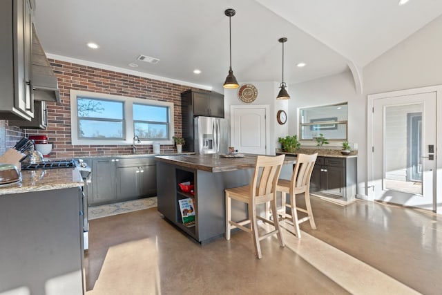 kitchen featuring a kitchen island, brick wall, appliances with stainless steel finishes, sink, and hanging light fixtures