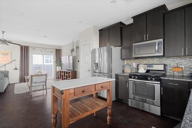 kitchen with stainless steel appliances, backsplash, light stone counters, ceiling fan, and dark wood-type flooring