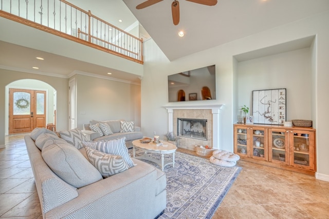 tiled living room featuring a high ceiling, a tile fireplace, ceiling fan, and crown molding