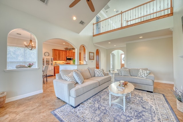 tiled living room featuring a high ceiling, crown molding, and ceiling fan with notable chandelier