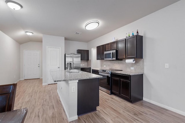 kitchen featuring sink, a center island with sink, appliances with stainless steel finishes, light stone countertops, and backsplash