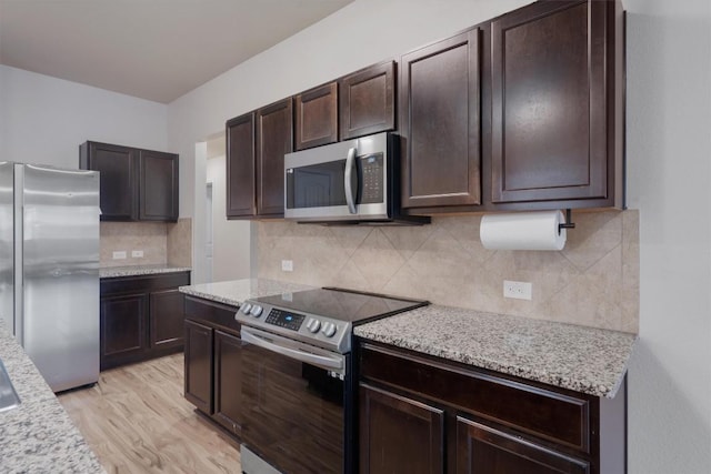 kitchen with light stone counters, appliances with stainless steel finishes, dark brown cabinets, and light wood-type flooring