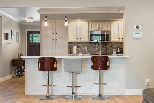 kitchen featuring hanging light fixtures, ornamental molding, a kitchen bar, decorative backsplash, and kitchen peninsula