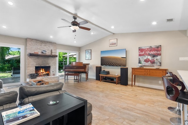 living room featuring ceiling fan, a stone fireplace, light hardwood / wood-style floors, and vaulted ceiling with beams