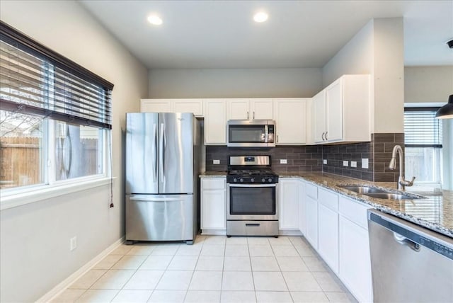 kitchen with sink, white cabinetry, stainless steel appliances, light stone counters, and light tile patterned flooring