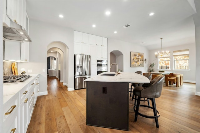 208 Wester Ross Ln, Austin, TX 78738 - kitchen featuring arched walkways, wall chimney exhaust hood, a center island with sink, and stainless steel appliances
