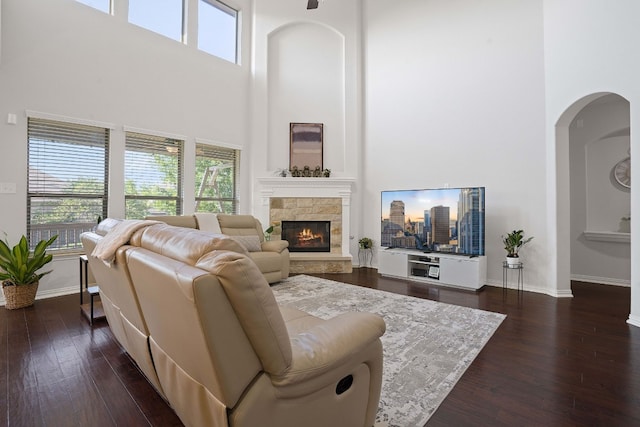 living room with dark wood-type flooring, a stone fireplace, and a high ceiling