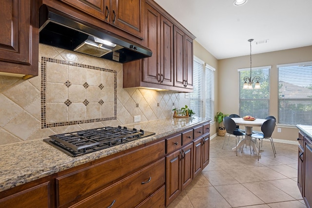 kitchen featuring a wealth of natural light, backsplash, stainless steel gas cooktop, light stone countertops, and an inviting chandelier