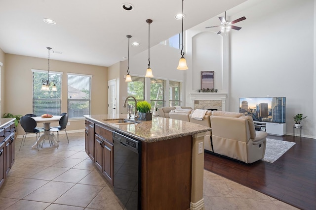 kitchen with pendant lighting, sink, a kitchen island with sink, black dishwasher, and light stone counters