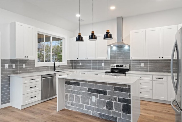 kitchen with a sink, appliances with stainless steel finishes, wall chimney range hood, light wood-type flooring, and backsplash