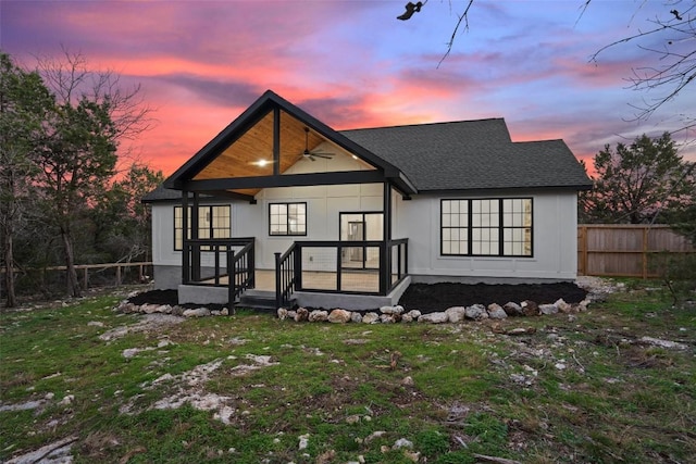 front of house at dusk featuring a lawn, roof with shingles, and fence