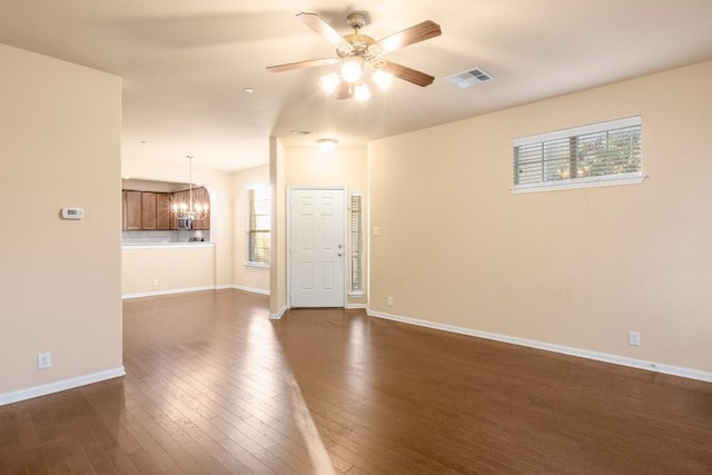 empty room with a healthy amount of sunlight, dark hardwood / wood-style floors, and ceiling fan with notable chandelier