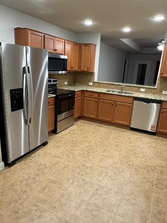 kitchen with light stone counters, sink, decorative backsplash, and appliances with stainless steel finishes