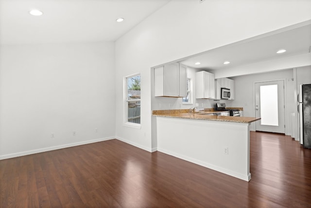 kitchen with dark wood-type flooring, kitchen peninsula, stainless steel appliances, light stone countertops, and white cabinets