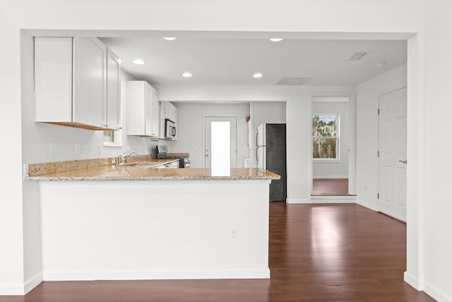 kitchen with appliances with stainless steel finishes, white cabinets, light stone counters, kitchen peninsula, and dark wood-type flooring