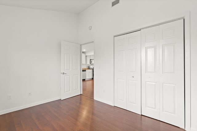 unfurnished bedroom with a high ceiling, dark hardwood / wood-style floors, and a closet