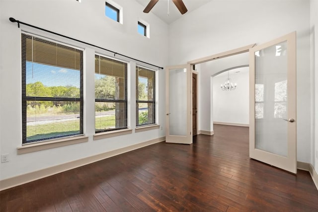 empty room featuring french doors, dark hardwood / wood-style flooring, ceiling fan with notable chandelier, and a high ceiling