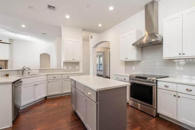 kitchen with appliances with stainless steel finishes, wall chimney exhaust hood, sink, and white cabinets