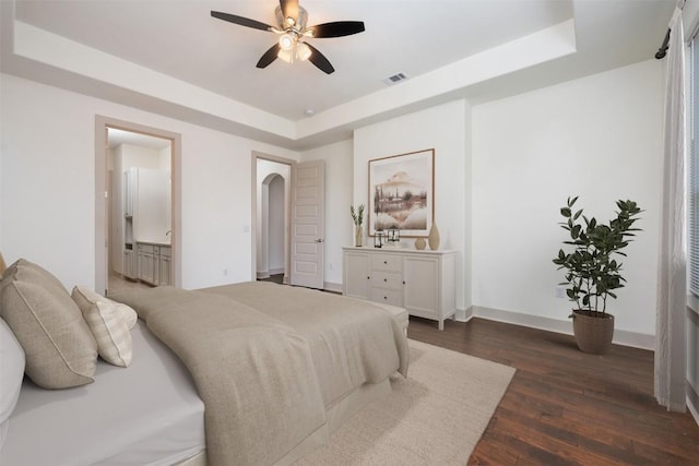 bedroom featuring dark hardwood / wood-style floors, ceiling fan, ensuite bathroom, and a tray ceiling