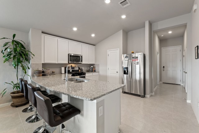 kitchen featuring a breakfast bar area, light stone counters, appliances with stainless steel finishes, kitchen peninsula, and white cabinets