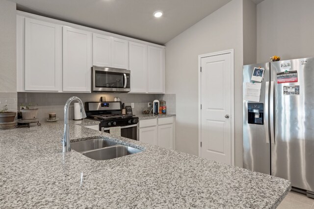 kitchen with white cabinetry, lofted ceiling, decorative backsplash, light stone counters, and stainless steel appliances