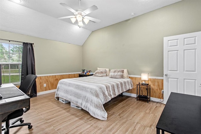 bedroom with ceiling fan, lofted ceiling, a textured ceiling, and wood walls